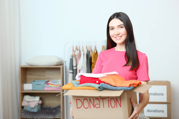 Молодая девушка-волонтер собирает коробку пожертвований для тех, кто нуждается во внутренней комнате
. - Фото, изображение
