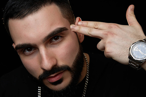 close-up of a dramatic portrait of a young serious guy, musician, singer, rapper with a beard in black clothes on a black isolated background. - Photo, Image
