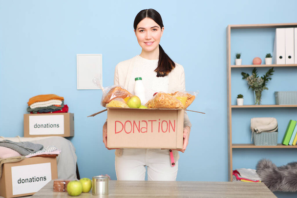 Een jonge meisje vrijwilliger verzamelt een doos met donaties voor degenen die behoefte hebben aan een interieur kamer. - Foto, afbeelding