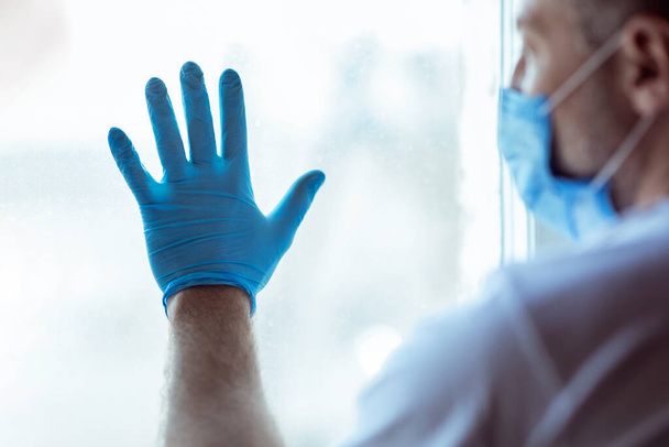 Sick Man Standing Near Window Wearing Medical Mask At Home - Foto, immagini