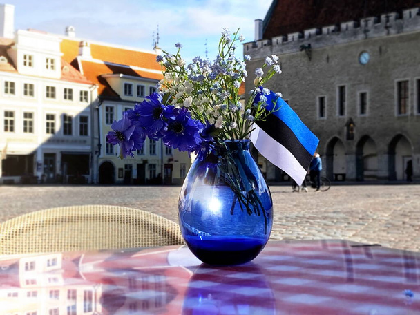 jarrón azul con flores y símbolos de la bandera de Estonia en la calle mesa de café Tallin casco antiguo medieval castillo hall plaza panorama hall plaza estonia
  - Foto, imagen