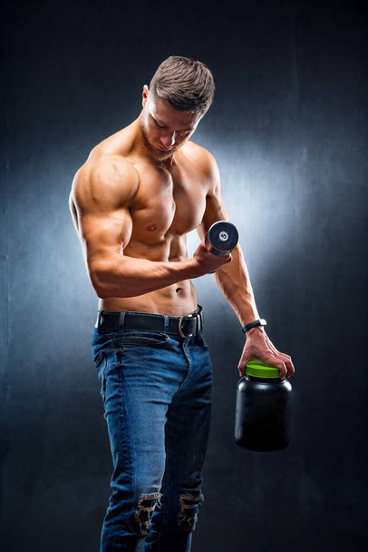 Young handsome muscular man with a sports nutrition and dumbbells in the hands. Dark blue background. - Fotó, kép