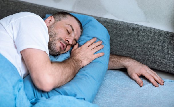 Man Sleeping Obejmuje poduszkę leżącą w łóżku w domu - Zdjęcie, obraz