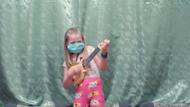 Meisje met een beschermend masker heeft plezier thuis tijdens de quarantaine. Gitaar spelen en zingen. - Video
