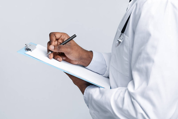 Ausschnitt aus afrikanischem Arzt füllt medizinisches Formular aus - Foto, Bild