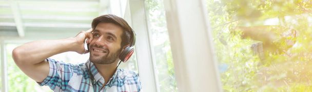 Junger Mann mit Kopfhörer steht zu Hause und hört Musik. - Foto, Bild