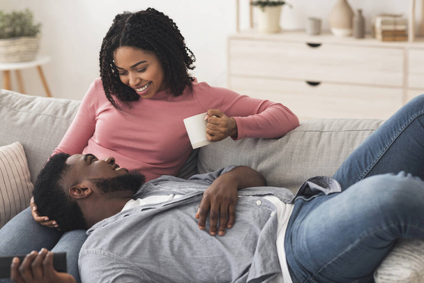 Fim de semana agradável. Casal afro-americano romântico relaxando no sofá em casa
 - Foto, Imagem
