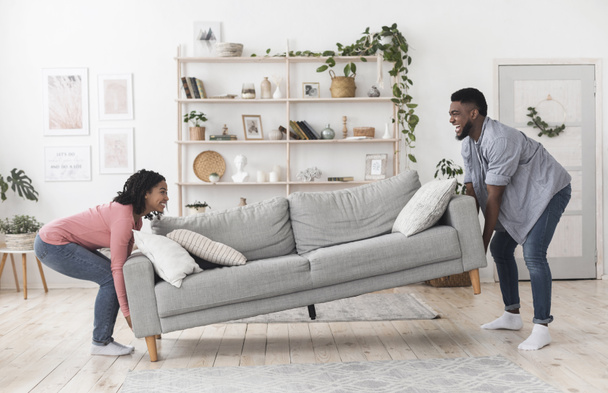 Schwarzes Paar zieht Sofa im Wohnzimmer um und ersetzt Möbel zu Hause - Foto, Bild