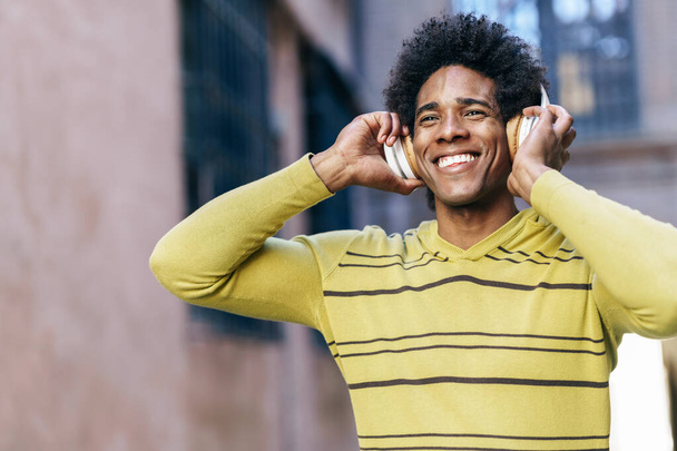 Black man listening to music with wireless headphones sightseeing in Granada - Fotó, kép