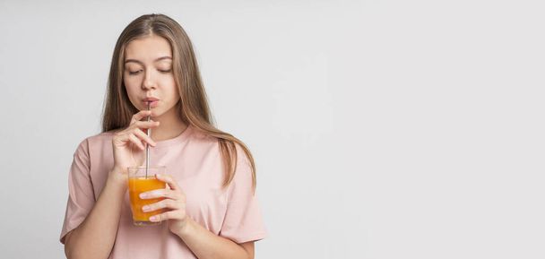 Happy young girl drinking orange infused water on white - Photo, Image