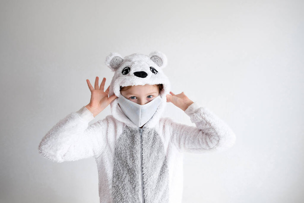  little girl in animal pajamas and protective face mask. a polar bear pajama is put on a child - Fotografie, Obrázek
