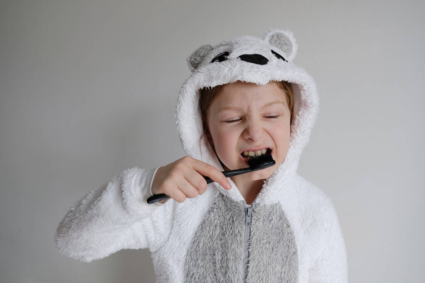 the little girl woke up in the morning and brushes her teeth with black coal toothpaste. The girl is wearing pajamas in the animal - Fotografie, Obrázek