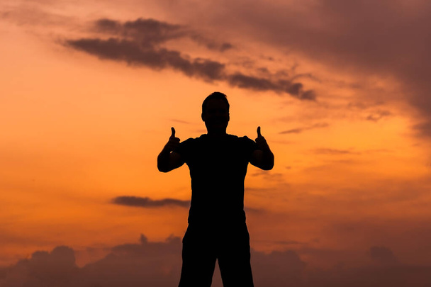 Silhueta de um homem com as mãos mostrando polegares para cima no pôr do sol, conceito empoderado
. - Foto, Imagem