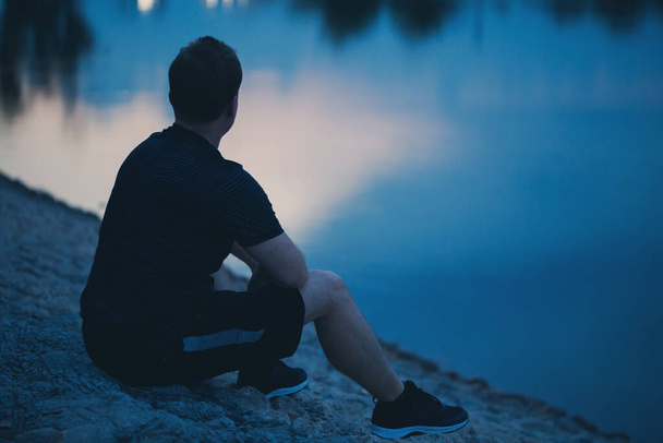 Junger Mann sitzt abends am Teich.  - Foto, Bild