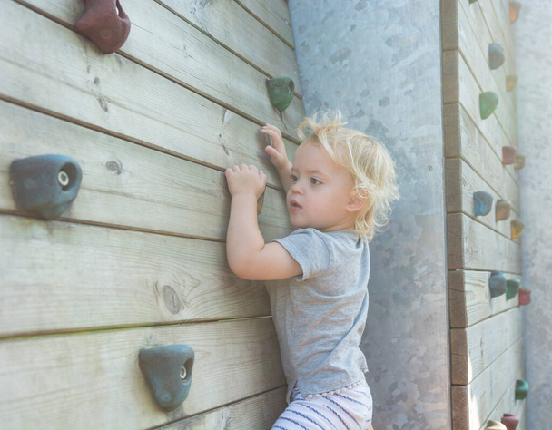 Porträt des niedlichen blonden Mädchens beim Klettern an einer Boulderwand im Freien. - Foto, Bild