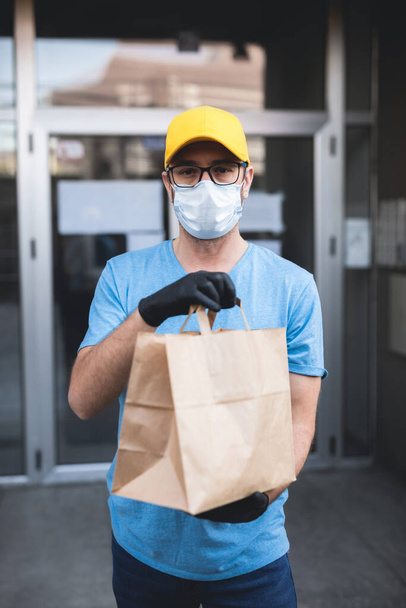 建物の前に食料品と保護マスクと手袋を保持ボックス/バッグを持つ配達人. - 写真・画像