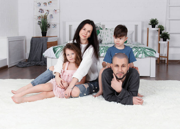 happy beautiful family in a bright home interior, laughing, smiling. mom dad son and daughter on a Studio photo shoot. in the bedroom and kitchen - Photo, Image