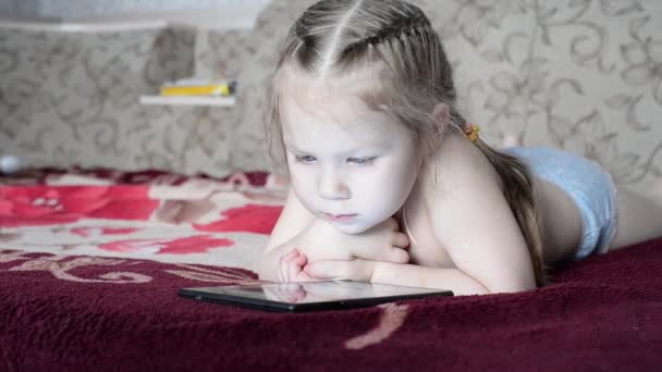 klein meisje kijken naar een smartphone terwijl liggend op een bank. - Video