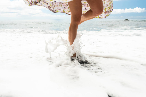 portrait woman standing on one leg by beach with water splashing on legs - Photo, Image