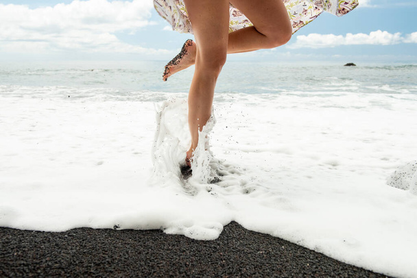 Боковой портрет женщины, стоящей на одной ноге у пляжа с брызгами воды на ногах
 - Фото, изображение
