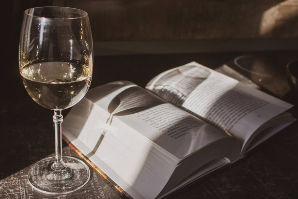 Open book and glass of white wine in sunlight filtered. Book and glass on table toned image. Literature concept. Home education concept. Read and study concept. Open book and glass of champagne in sunshine. - Foto, Imagem
