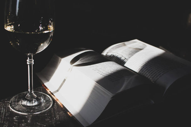 Open book and glass of white wine in sunlight filtered. Book and glass on table toned image. Literature concept. Home education concept. Read and study concept. Open book and glass of champagne in sunshine. - Fotografie, Obrázek