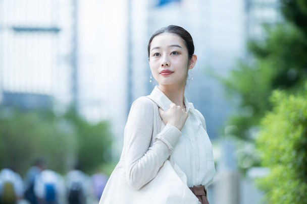 カジュアルな服装でビジネス街へ通勤するアジア系ビジネス女性 - 写真・画像