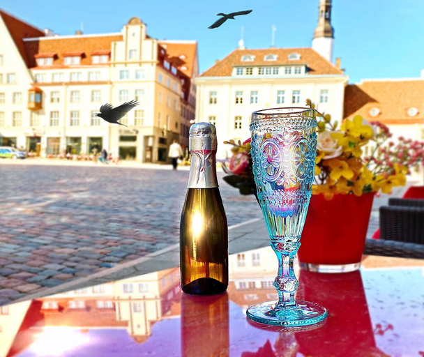 μπουκάλι σαμπάνια ποτήρι σαμπάνια δρόμο καφέ Ταλίν παλιά πλατεία Δημαρχείο Εσθονία άνοιξη λουλούδια τριαντάφυλλα μπουκέτο κόκκινο βάζο στο τραπέζι κορυφή πόλη πανόραμα πουλιά πετούν μπλε ουρανό μεσαιωνική πόλη καλοκαίρι  - Φωτογραφία, εικόνα