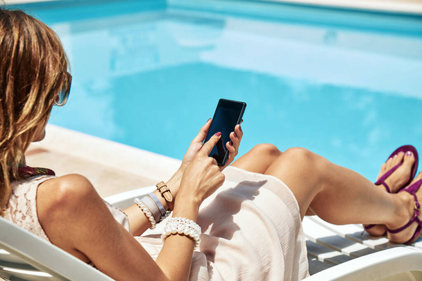 Young woman using cellphone near the swimming pool. - Photo, Image