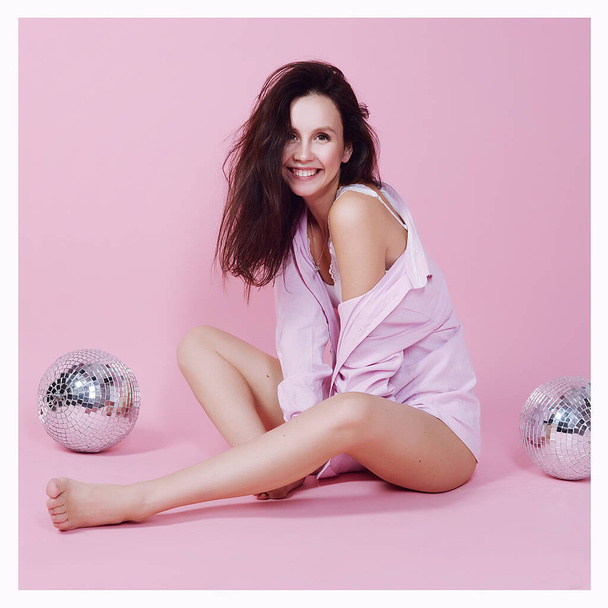 cute girl in a shirt on a pink background having fun and fooling around with a disco ball - Foto, afbeelding