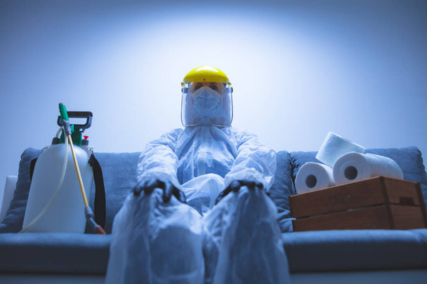Osoba z kolbą papieru toaletowego i ochronną maską przeciwwirusową, skafandrem, hełmem i chemicznym rozpylaczem w izolacji domowej. - Zdjęcie, obraz