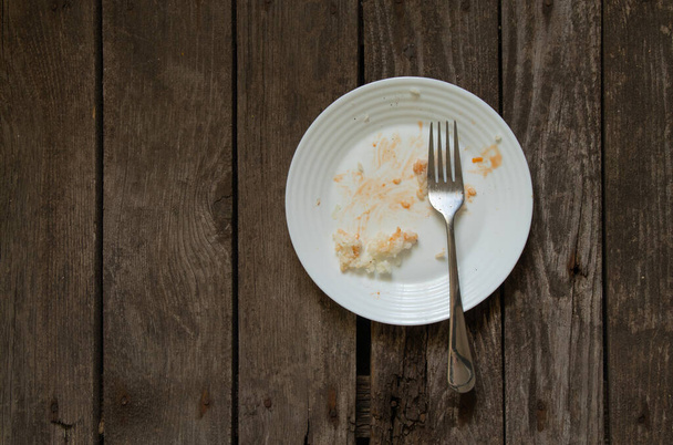 ένα λευκό βρώμικο πιάτο με περισσευούμενο φαγητό μετά το γεύμα στέκεται σε μια ξύλινη σανίδα - Φωτογραφία, εικόνα
