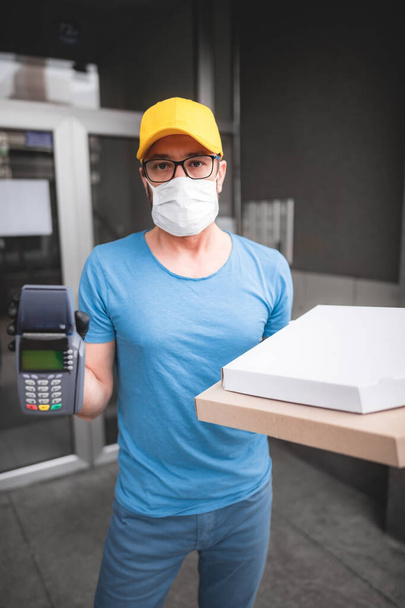 Repartidor con máscara médica protectora sosteniendo la caja de pizza - días de virus y pandemia, entrega de alimentos a su hogar
. - Foto, Imagen