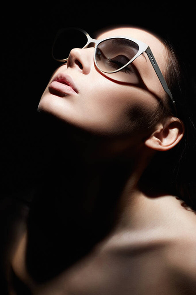 egy gyönyörű nő portréja szemüvegben. Retro stílusú portré. Lady Girl néz a sötétségből - Fotó, kép