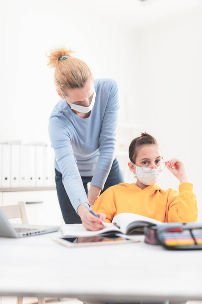 Child home studying education, homeschooling, with private tutor / mother with protective mask in the time of viruses, flu and seasonal pandemic, healthy approach in social contact. - Photo, Image