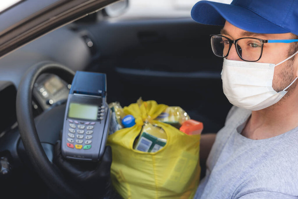 Доставщик в защитной маске и перчатках, покрывающий продукты во время блокировки и пандемии
. - Фото, изображение