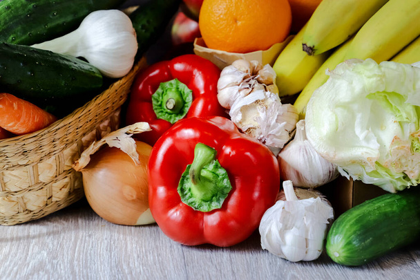 Close-up of red pepper, garlic, cucumber, Iceberg salad, a basket of cucumbers and fresh garlic, bananas and an orange. Still life, composition of fresh vegetables. - Foto, Imagen
