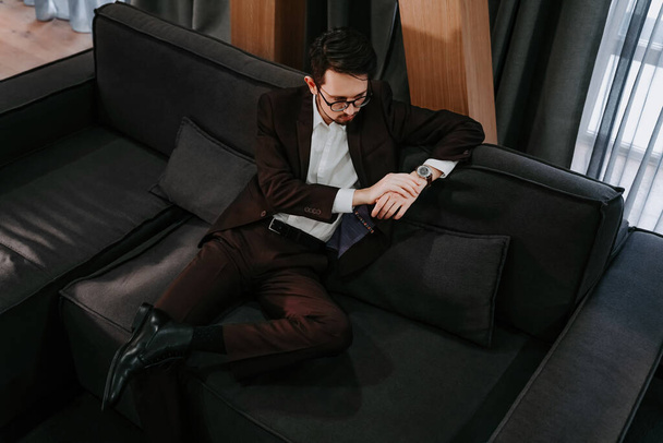 Ένας κουρασμένος άντρας μετά τη δουλειά ξεκουράζεται σε έναν καναπέ στο σπίτι. Επιχειρηματίας μετά από διαπραγματεύσεις - Φωτογραφία, εικόνα