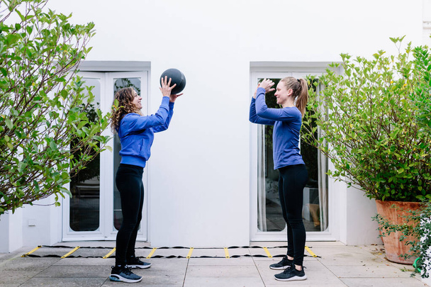 Kaksi nuorta naista tekee liikuntaa yhdessä lääkepallon kanssa terassilla
 - Valokuva, kuva