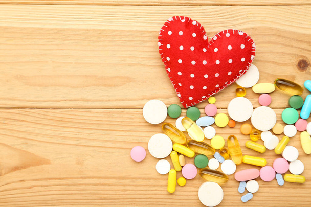 Doctor's Day concept. Red fabric heart with colorful pills on wooden table - Zdjęcie, obraz