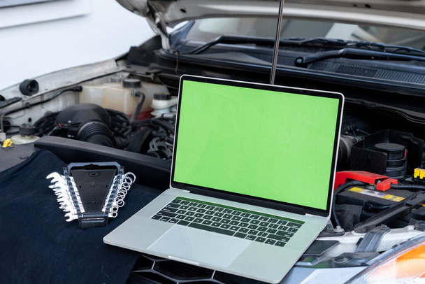 Laptopcomputer op motorkap voor motordiagnose. Auto garage reparatie service concept. - Foto, afbeelding