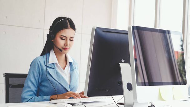 Customer support agent or call center with headset works on desktop computer while supporting the customer on phone call. Operator service business representative concept. - Photo, image
