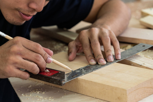 Carpinteiro trabalhando em artesanato de madeira na oficina para produzir material de construção ou móveis de madeira. O jovem carpinteiro asiático usa ferramentas profissionais para artesanato. DIY maker e conceito de trabalho de carpintaria. - Foto, Imagem