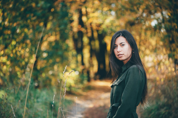 Female beauty portrait surrounded by vivid foliage. Dreamy beautiful girl with long natural black hair on autumn background with colorful leaves in bokeh. Inspired girl enjoys nature in autumn forest. - Photo, Image