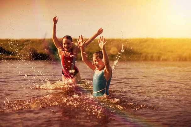 kleine meisjes in gekleurde zwempakken spetteren in rivier in dorp - Foto, afbeelding