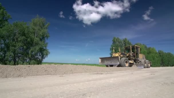 Cesta funguje. Traktor vyrovnává půdu ve venkovské krajině. - Záběry, video