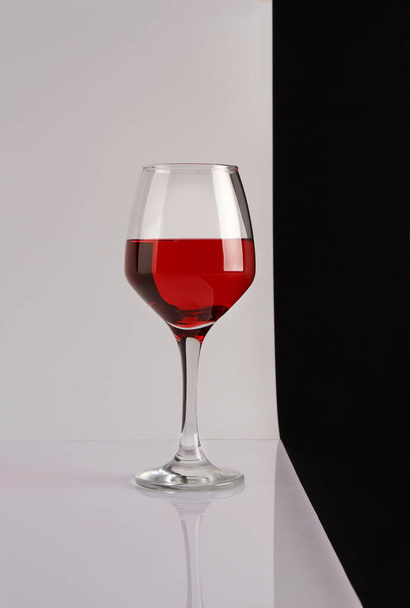 Still life with a glass of red wine on a white glossy table and black and white background - Foto, Imagen