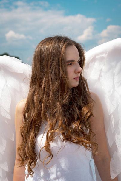 Een groot portret van een mooi meisje met lang haar in het beeld van een engel met witte vleugels. - Foto, afbeelding