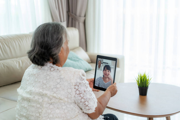 Asiática anciana virtual happy hour encuentro y hablar en línea junto con su hija en videoconferencia con tableta digital para una reunión en línea en videollamada para distanciamiento social
 - Foto, Imagen
