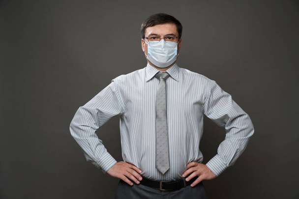a man dressed as a businessman posing in a studio on a gray background, medical face mask, glasses, a light striped shirt and tie - casual office wear, concept of quarantine and antivirus protection - Fotoğraf, Görsel